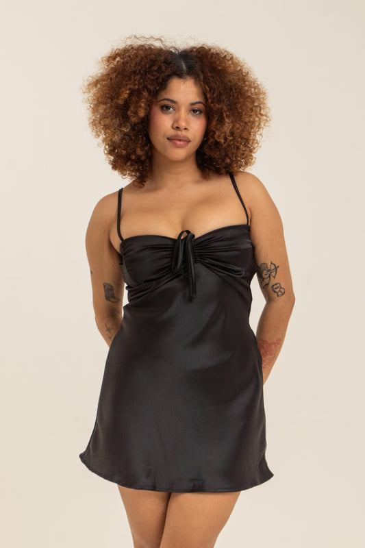 modelo com vestido mini plus size preto, todo em cetim. O look perfeito pro seu date